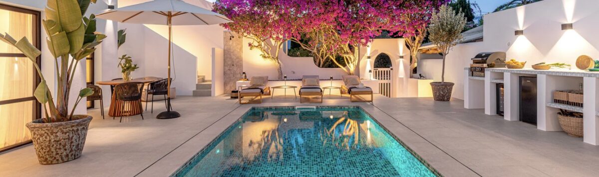 Traumvilla Sol de Mallorca: Beleuchteter Pool mit Mosaikfliesen, Bougainvillea und Außenküche im Abendlicht.