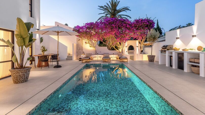 Traumvilla Sol de Mallorca: Beleuchteter Pool mit Mosaikfliesen, Bougainvillea und Außenküche im Abendlicht.