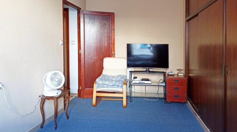 Wohnzimmer mit blauem Teppich, Sessel, Flachbild-TV und großem Holzschrank in Palma de Mallorca