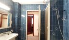 Badezimmer mit blauen Fliesen, Waschbecken, Dusche und Spiegel – renovierungsbedürftig, aber funktional.