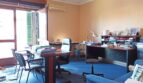 Bürozimmer mit blauem Teppich, zwei Schreibtischen, Klimaanlage und großem Fenster mit Fensterläden.