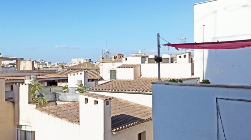 Dachterrassen-Ausblick auf weiße Altstadt-Gebäude mit Ziegeldächern unter blauem Himmel in Palma de Mallorca