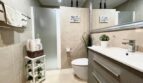 Modernes Badezimmer mit beiger Fliesenverkleidung, Glasdusche, Wandhänge-WC und elegantem Holzwaschtisch in Llucmajor.