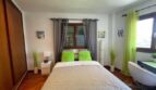 Helles Schlafzimmer mit Doppelbett, grünen Akzenten, Holzboden und Einbauschrank im Einfamilienhaus Llucmajor