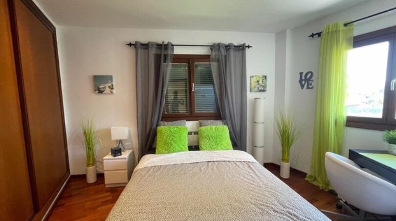 Helles Schlafzimmer mit Doppelbett, grünen Akzenten, Holzboden und Einbauschrank im Einfamilienhaus Llucmajor