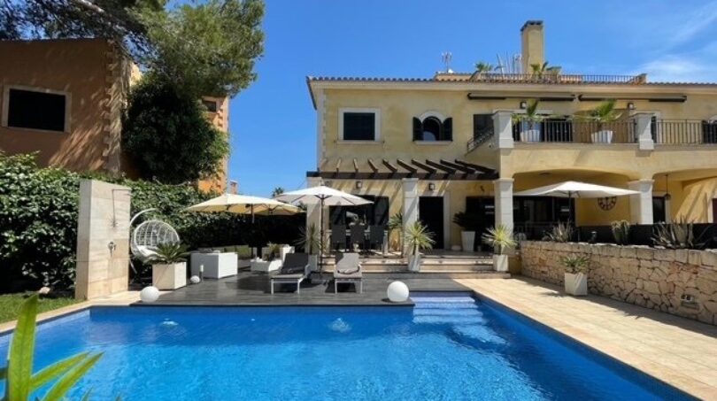 Außenansicht: Mediterrane Villa in Llucmajor mit blauem Pool, Sonnenterrasse und Lounge-Bereich unter Sonnenschirmen.