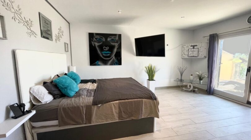 Helles Schlafzimmer mit Doppelbett, türkisen Kissen, Wandkunst, TV und Terrassenzugang in Llucmajor