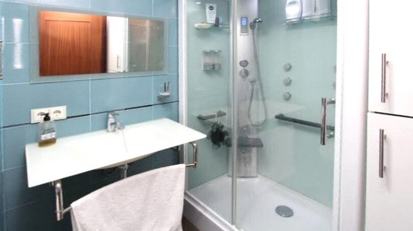 Modernes Badezimmer mit Glasdusche, Wandspiegel und blauer Fliesenverkleidung in exklusiver Hafenwohnung El Toro