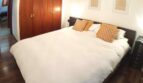 Schlafzimmer mit Doppelbett, weißer Bettwäsche, goldenen Kissen, Holzschrank und Parkettboden in Wohnung Port Adriano