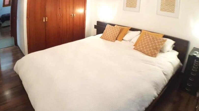 Schlafzimmer mit Doppelbett, weißer Bettwäsche, goldenen Kissen, Holzschrank und Parkettboden in Wohnung Port Adriano