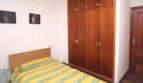 Schlafzimmer mit Einzelbett, gelbem Streifenbezug, großem Holzschrank und Buddha-Wandbildern in Port Adriano