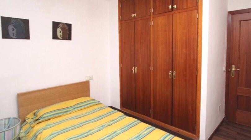 Schlafzimmer mit Einzelbett, gelbem Streifenbezug, großem Holzschrank und Buddha-Wandbildern in Port Adriano