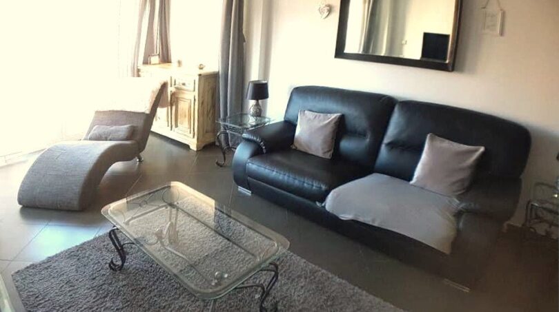 Elegantes Wohnzimmer mit schwarzem Ledersofa, Glascouchtisch und Spiegel in exklusiver Hafenwohnung El Toro