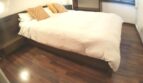 Modernes Schlafzimmer mit Doppelbett, goldenen Akzentkissen und Holzparkett in exklusiver Wohnung am Yachthafen.