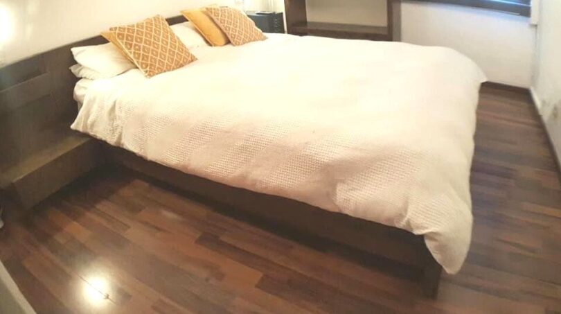 Modernes Schlafzimmer mit Doppelbett, goldenen Akzentkissen und Holzparkett in exklusiver Wohnung am Yachthafen.