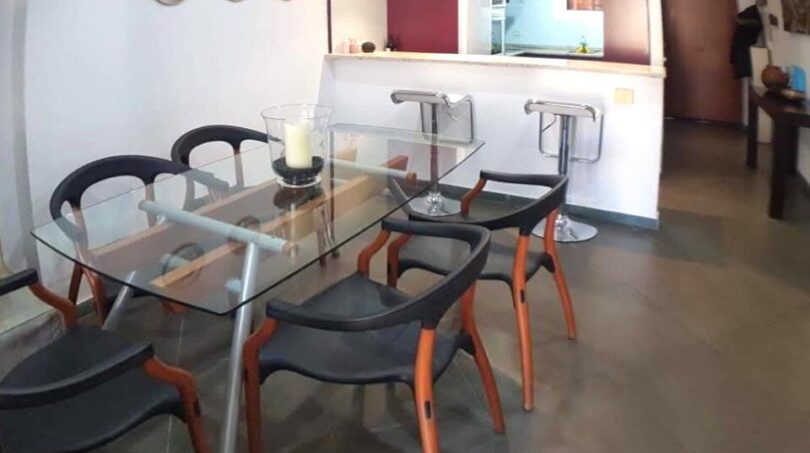 Modernes Esszimmer mit Glastisch und schwarzen Designerstühlen, Blick auf offene Küche in Wohnung Port Adriano