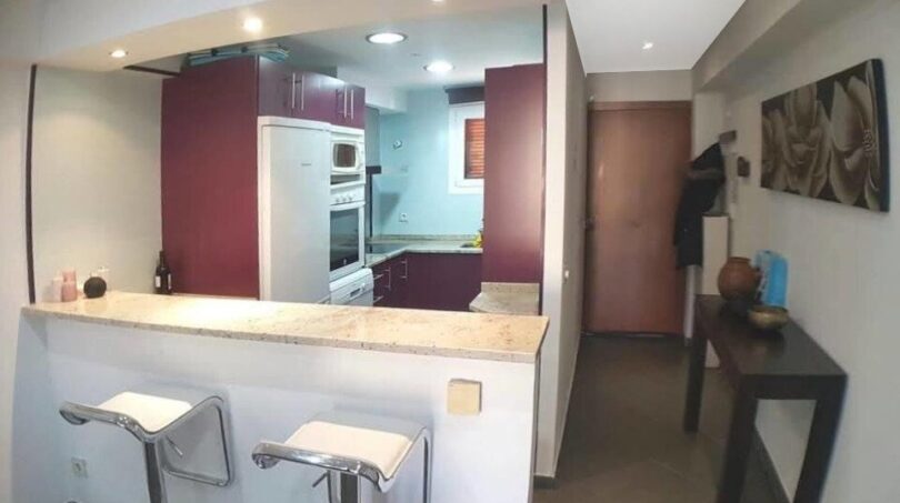 Offene Küche mit lila Fronten, Marmor-Theke und zwei Barhockern in exklusiver Wohnung in Port Adriano
