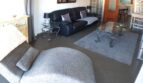 Elegantes Wohnzimmer mit schwarzem Ledersofa, Glastisch und grauem Sessel in exklusiver Hafenwohnung Port Adriano