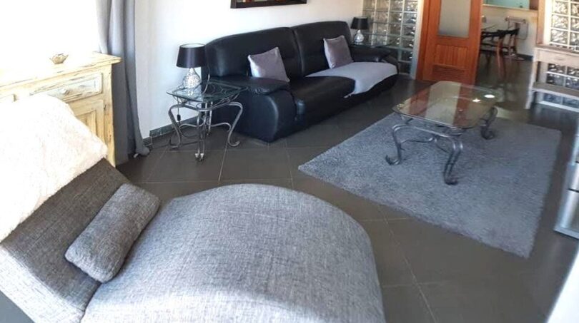 Elegantes Wohnzimmer mit schwarzem Ledersofa, Glastisch und grauem Sessel in exklusiver Hafenwohnung Port Adriano
