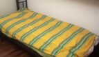Einzelbett mit gelb-grün gestreifter Bettwäsche in schlichtem Schlafzimmer mit Holzboden, Wohnung Port Adriano