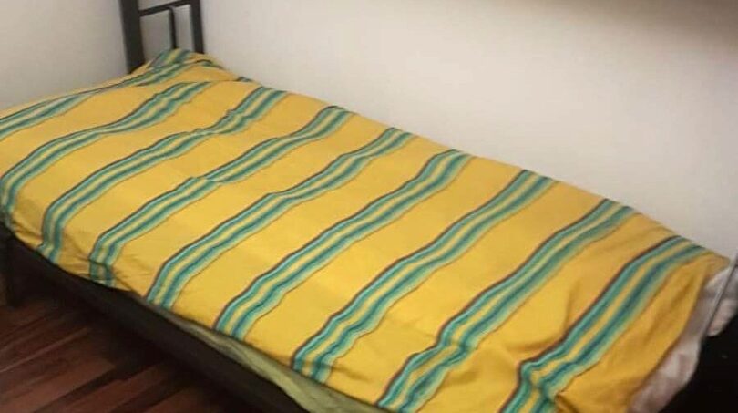 Einzelbett mit gelb-grün gestreifter Bettwäsche in schlichtem Schlafzimmer mit Holzboden, Wohnung Port Adriano