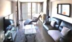 Modernes Wohnzimmer mit Ledersofa, Glastisch, TV und Balkonzugang in exklusiver Wohnung am Yachthafen Port Adriano