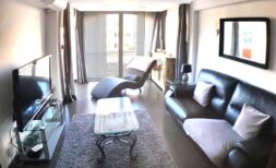 Modernes Wohnzimmer mit Ledersofa, Glastisch, TV und Balkonzugang in exklusiver Wohnung am Yachthafen Port Adriano