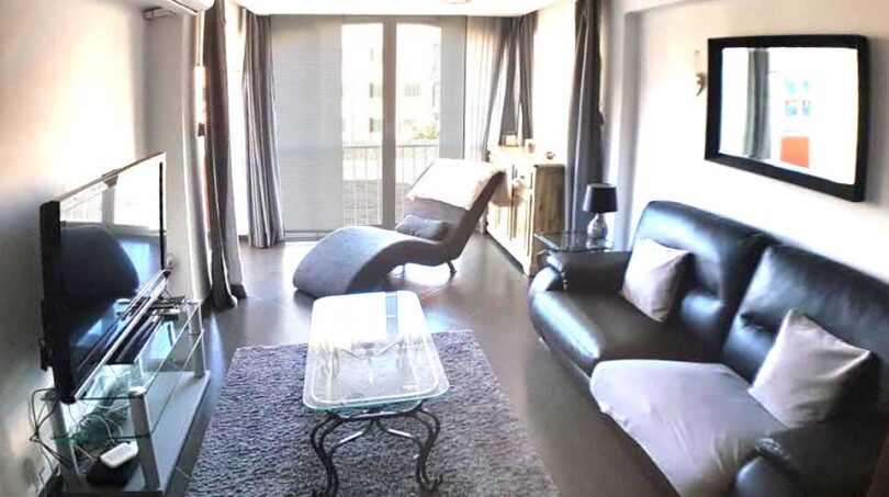Modernes Wohnzimmer mit Ledersofa, Glastisch, TV und Balkonzugang in exklusiver Wohnung am Yachthafen Port Adriano