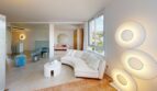 Helles Wohnzimmer mit geschwungenem weißem Sofa, runden Wandleuchten und Meerblick in Luxuswohnung Illetas