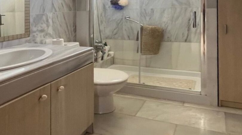 Helles Badezimmer mit Marmorverkleidung, Glasdusche, WC und Holzunterschrank im Reihenhaus Llucmajor