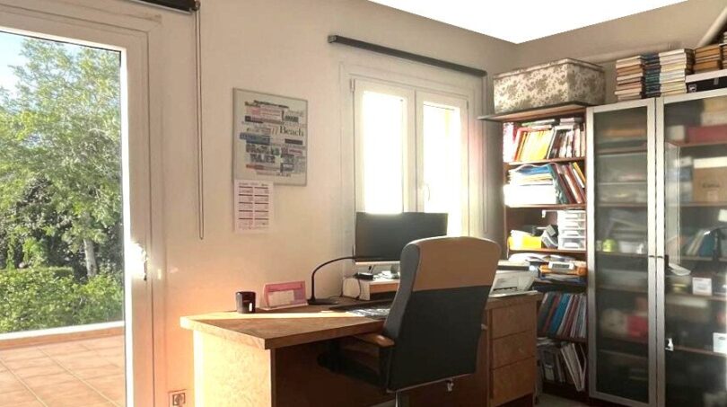 Helles Arbeitszimmer mit Holzschreibtisch, Bücherregal und großem Fenster mit Balkonzugang im Reihenhaus Llucmajor.