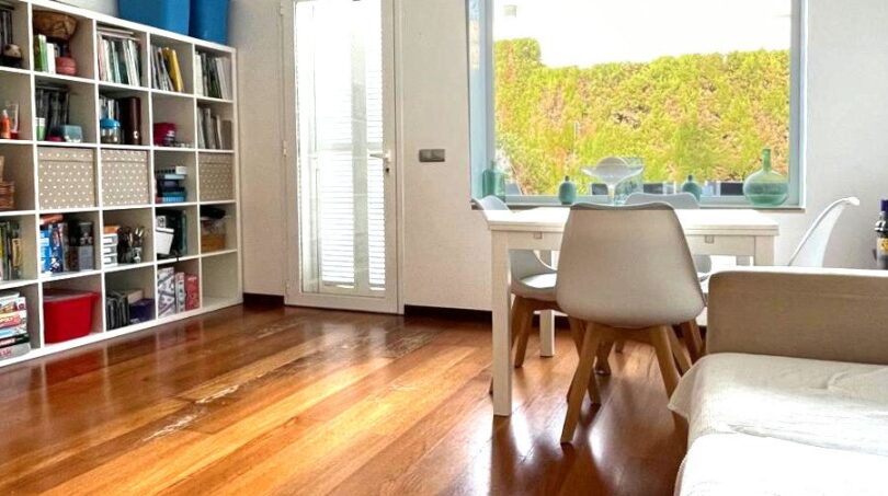 Helles Wohnzimmer mit Holzboden, Bücherregal und Gartenblick im modernen Reihenhaus in Llucmajor.