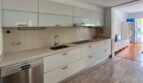 Moderne weiße Einbauküche mit Granitboden, Induktionskochfeld und Edelstahlspüle im Reihenhaus Llucmajor