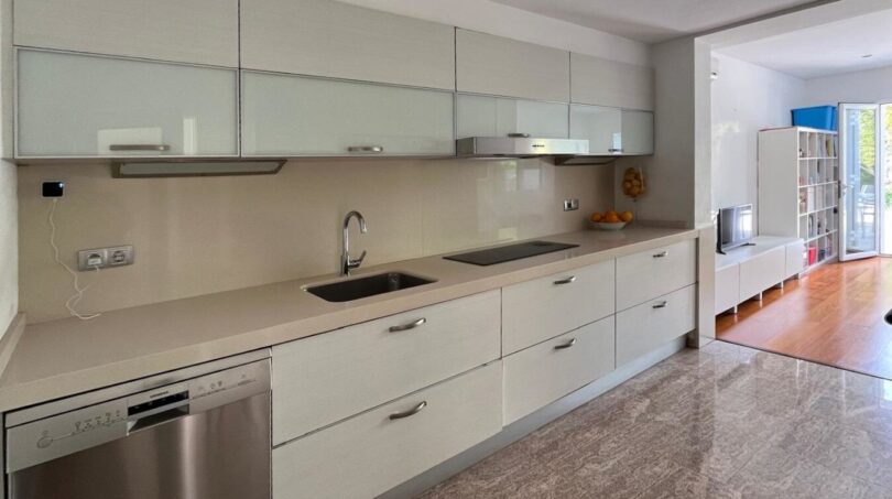 Moderne weiße Einbauküche mit Granitboden, Induktionskochfeld und Edelstahlspüle im Reihenhaus Llucmajor
