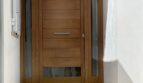 Eingangsbereich des Reihenhauses in Llucmajor mit moderner Holztür, Glasseiten, Designerlampe und Natursteintreppe.