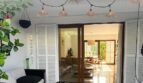 Überdachte Terrasse mit Rattanleuchten, schwarzem Sofa und Glastür zum Innenbereich des Reihenhauses in Llucmajor.
