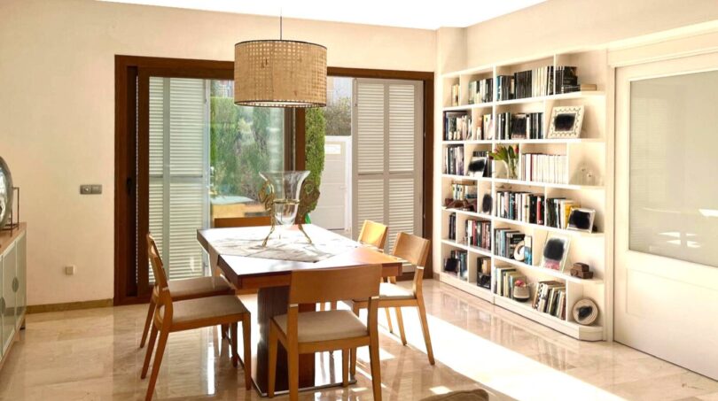 Helles Esszimmer mit Marmorboden, Holztisch, Stühlen, Bücherregal und Gartenblick im Reihenhaus Llucmajor