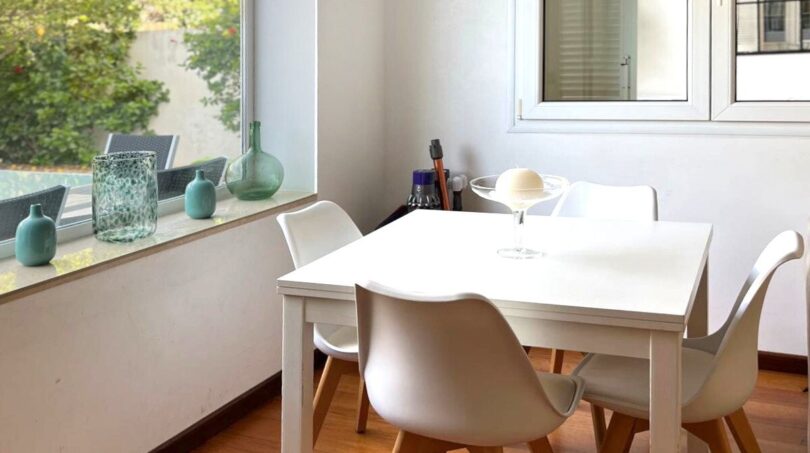 Helles Esszimmer mit weißem Tisch, modernen Stühlen, Holzboden und großem Fenster mit Grünblick.