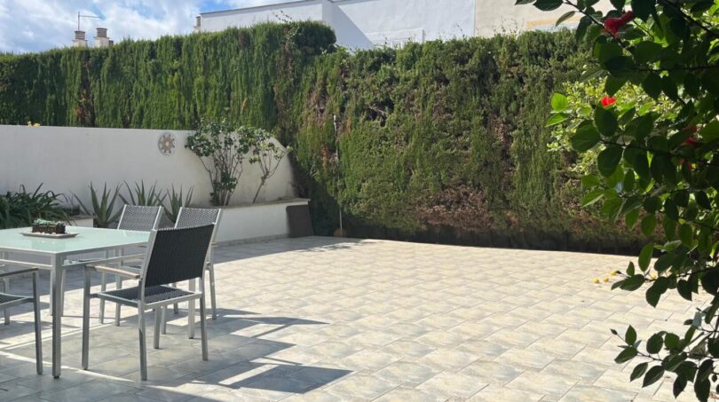 Sonnige Terrasse mit Gartenmöbeln, Fliesenboden und hoher Hecke beim Reihenhaus in Llucmajor
