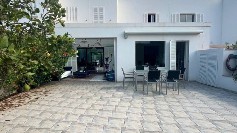Sonnige Terrasse mit Esstisch und Stühlen, Markise und großen Glastüren zum Wohnbereich, weißes Reihenhaus Llucmajor