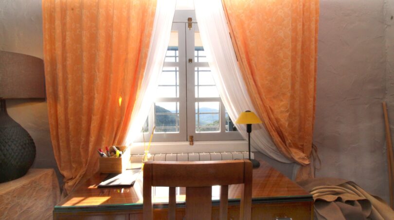 Schreibtisch mit Holzstuhl vor Fenster mit orangefarbenen Vorhängen und Meerblick in Berganwesen Esporles