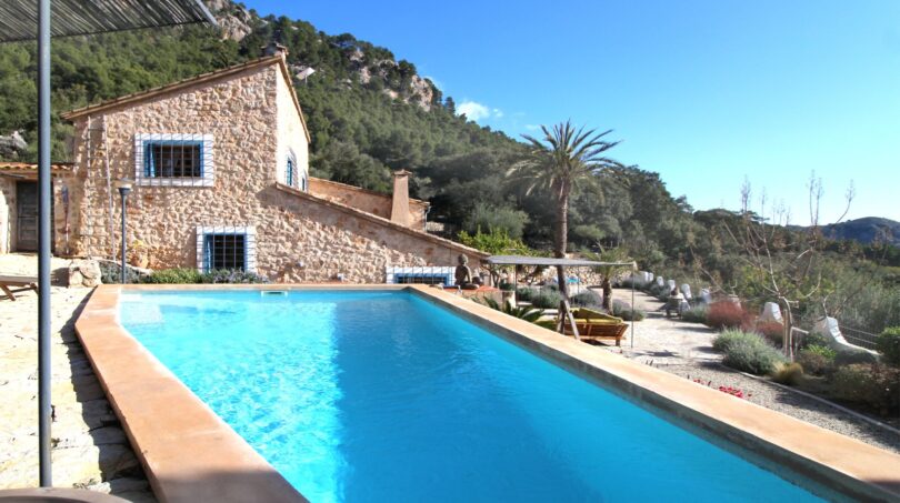 Außenpool einer Finca in Esporles mit Natursteinhaus, Palme und Bergpanorama