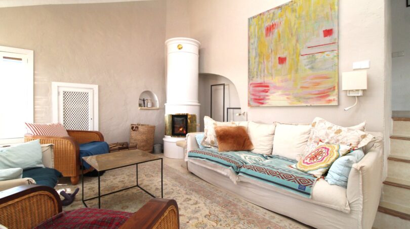 Helles Wohnzimmer mit weißem Kachelofen, gemütlichem Sofa und farbenfrohem Kunstwerk in Bergjuwel Esporles