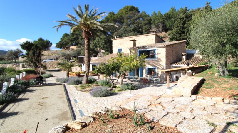 Rustikale Finca in Esporles mit Natursteinmauern, Palme, mediterranem Garten und gepflastertem Innenhof.