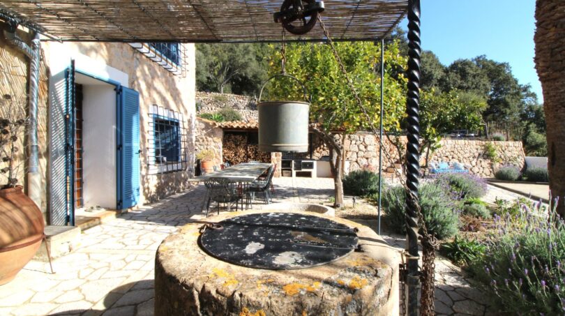 Rustikaler Innenhof mit antikem Steinbrunnen, Pergola und blauem Fensterläden in Bergjuwel Esporles