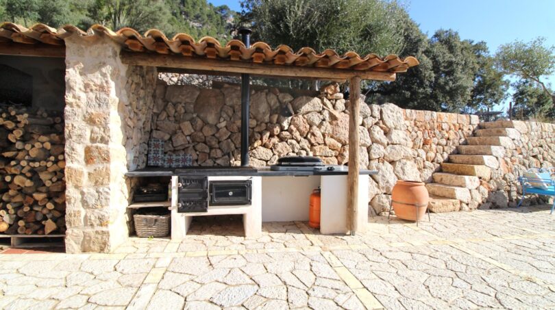 Rustikale Außenküche mit Steinmauern, Holzofen und Terrakottafliesen der Berghütte in Esporles
