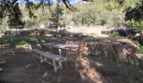 Rustikaler Außensitzbereich mit Holzbank und Rattanstuhl, umgeben von Natursteinmauern und Eichen in Esporles.