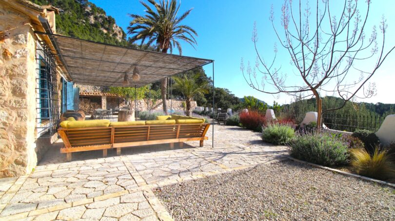 Mediterrane Terrasse mit Natursteinboden, Loungesofa und Pergola, umgeben von Palmen und Bergkulisse in Esporles.