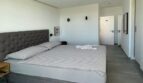 Helles Schlafzimmer mit Doppelbett, gepolstertem Kopfteil, Deckenventilator und großen Bodenfliesen in Meeresnähe.