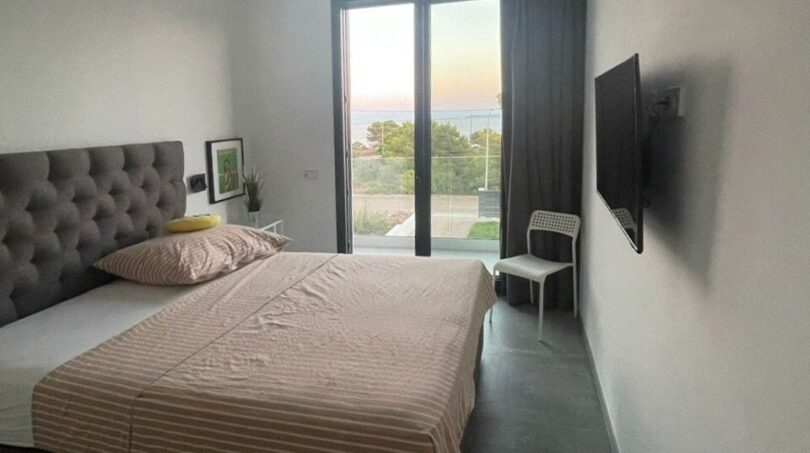 Modernes Schlafzimmer mit Doppelbett, Deckenventilator, Wand-TV und Meerblick durch Terrassentür in Cala Pi.